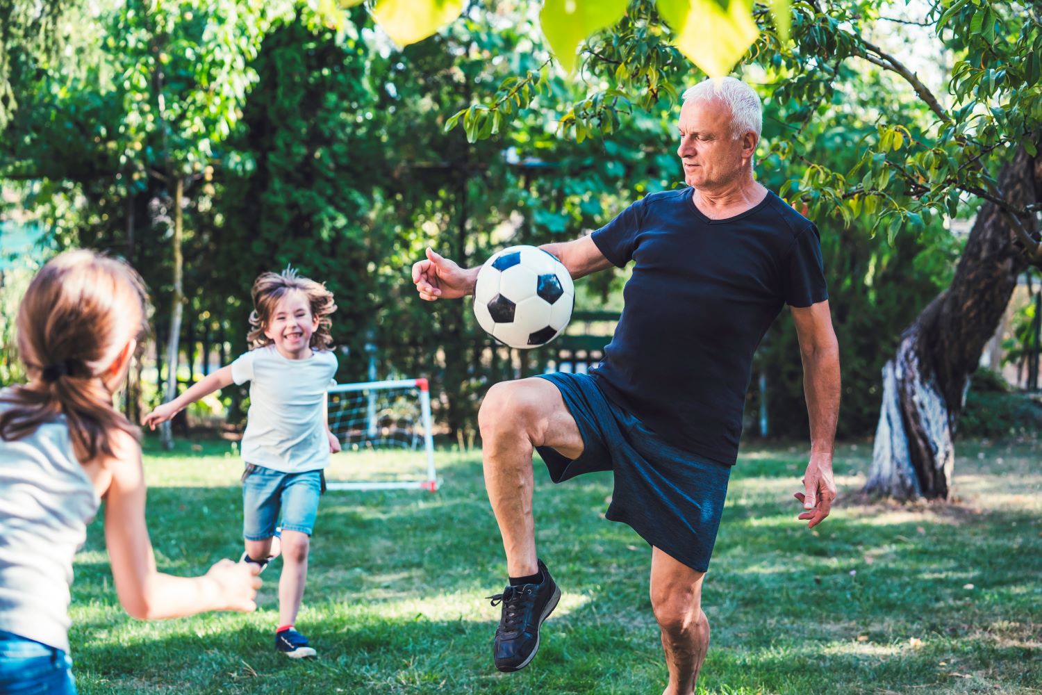 A man plays football with his grandchildren; ?>